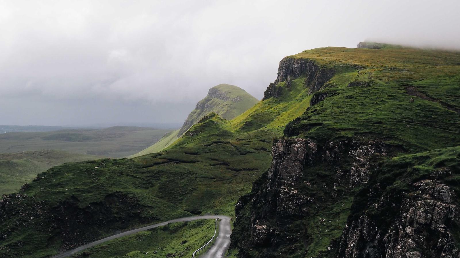 Winding road through lush green misty highland hills